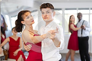 Pretty young woman dancing waltz with partner at group of multinational people in ballroom dancing class