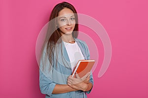 Pretty young woman with dark straight hair standing with note book inhands, writing, take notes, holding textbook organizer,