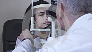 Pretty young woman do eye test at clinic sitting in front of doctor in white medical coat looking in eye test machine