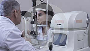 Pretty young woman do eye test at clinic sitting in front of doctor in white medical coat looking in eye test machine