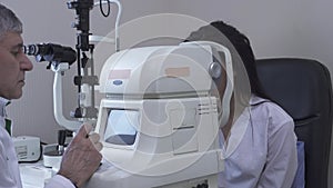 Pretty young woman do eye test at clinic sitting in front of doctor in white medical coat looking in modern eye test