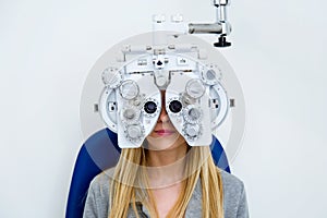 Pretty young woman doing eyesight measurement with optical phoropter in ophthalmology clinic