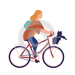 Pretty young woman dressed in casual clothes riding bike with cat sitting in basket. Cute girl on bicycle with her pet