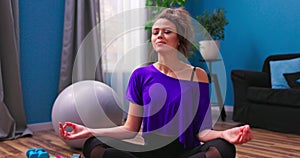 A pretty young woman dressed in fitness clothes meditates while sitting in lotus position on