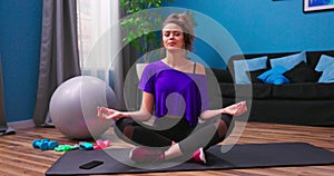 A pretty young woman dressed in fitness clothes meditates while sitting on a wooden floor