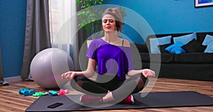 A pretty young woman dressed in fitness clothes meditates while sitting on a wooden floor