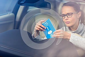 Pretty, young woman driving her new car - putting the necessary parking clock behind the windshield