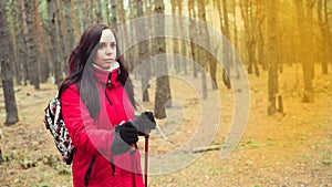 A pretty young woman is engaged in the nordic walking in woods.