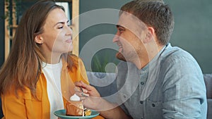 Pretty young woman enjoying cake and laughing while guy is feeding her at home