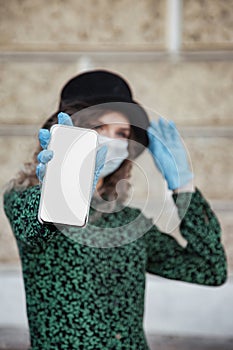 Pretty young woman in French style in medical mask and gloves show mobile phone