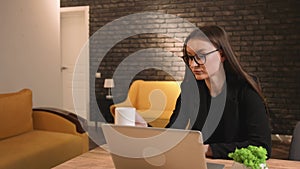 Pretty young woman in glasses with a cup of coffee, using laptop, has video call chatting, woman chatting on laptop