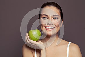 Pretty young woman with green apple smiling on brown background