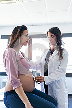 Pretty young woman gynecologist checking the heartbeat baby of her pregnant patient in the clinic