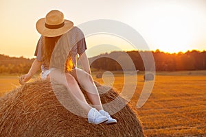 Pretty young woman in hat sitting on a hay bale