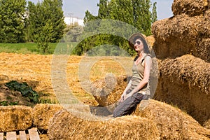 Pretty happy woman with hat sitting on straw bales and getting some rest.