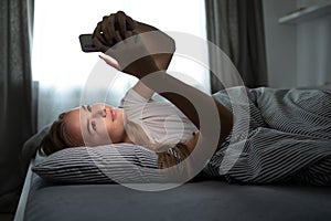 Pretty, young woman in her bed with her cell phone