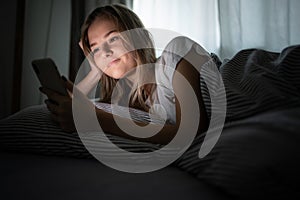 Pretty, young woman in her bed with her cell phone