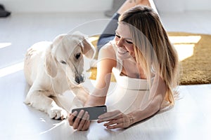 Pretty young woman with her dog using mobile phone while lying on the floor at home