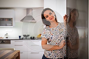 Pretty, young woman in her modern kitchen, by the fridge