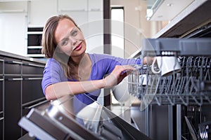 Pretty, young woman in  kitchen putting cups into the dishwasher