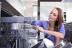 Pretty, young woman in  kitchen putting cups into the dishwasher