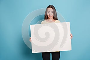 Pretty young woman holding empty blank board over blue background