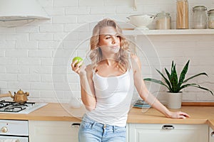 Pretty young woman holding green apple and smiling at home kitchen, diet and healthy eating concept