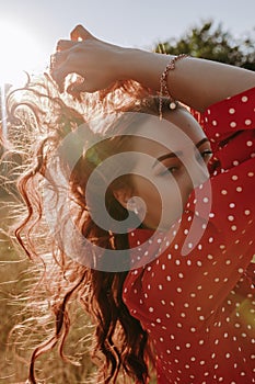 Pretty young woman holding her hair by hands and posing on a camera on the middle of wheat field