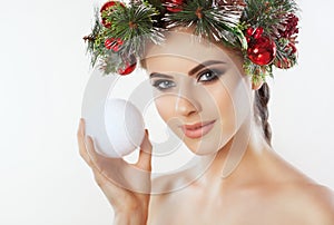 A pretty young woman holds in her hand a Christmas ball, on her head a beautiful wreath of spruce with cones and balls