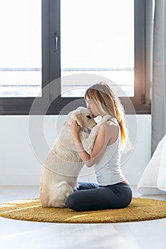 Pretty young woman hugging her dog while sitting on the floor at home