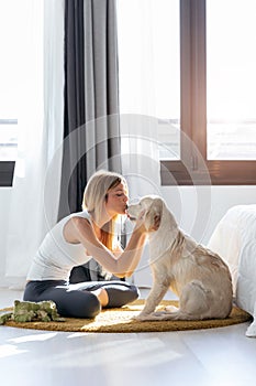 Pretty young woman kissing her dog while sitting on the floor at home