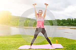 Pretty young woman lifting small weights dumbbells in the park