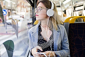 Pretty young woman listening to music with mobile phone at the bus.