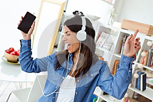 Pretty young woman listening to music with mobile phone while dancing in the living room at home