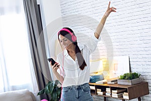 Pretty young woman listening to music with mobile phone while dancing in the living room at home