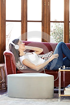 Pretty young woman listening to music while relaxing on couch at home