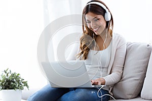 Pretty young woman listening to music while using her laptop at home.