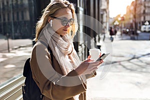 Pretty young woman listening to music with wireless earphones and the smartphone in the street