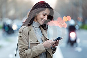 Pretty young woman listening to music with wireless earphones and the smartphone in the street