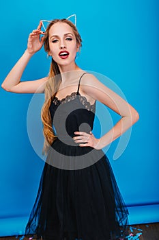 Pretty young woman with long blonde hair on party, masquerade, carnival posing to camera at blue background. Wearing