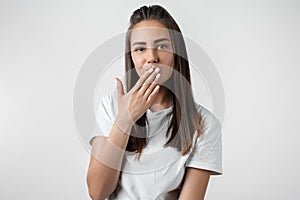 Pretty young woman with long chestnut hair dressed in casual clothes covering mouth. Keep silence concept