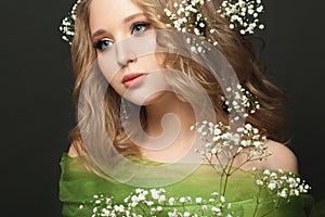 Pretty young woman with long healthy curly hair and white flowers on black background, beautiful face close up