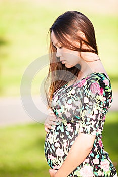 Pretty young woman looking down adoring her pregnant stomach in a beautiful green park background