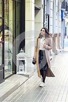 Pretty young woman looking at a shop window while walking in the street