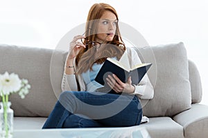 Lindo mujer joven buscando aparte mientras lectura un libro sobre el sofá sobre el 