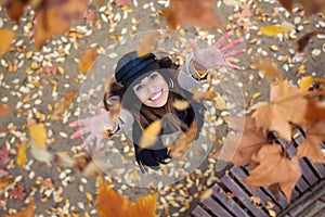 Pretty young woman looking to the sky with arms raised as leaves fall from the trees in the park in autumn