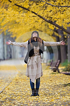 Pretty young woman looking to sky with arms raised and having fun in the park in autumn