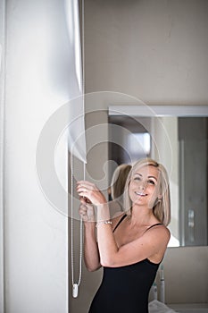 Pretty, young woman lowering the interior shades/blinds