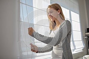 Pretty, young woman lowering the interior shades/blinds