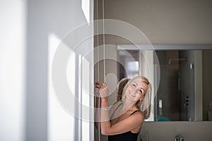 Pretty, young woman lowering the interior shades/blinds photo